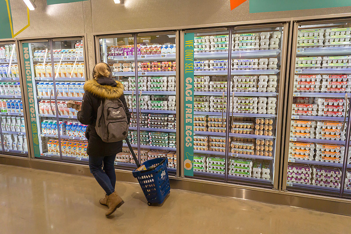 Woman in a grocery store walking by the refrigerated section full of eggs and milk.