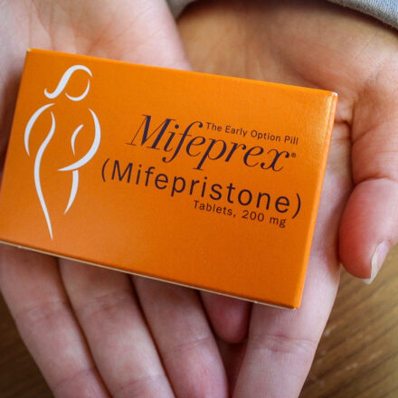 Two hands holding up a box of mifeprex, the abortion pill
