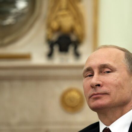 Head shot of Vladimir Putin looking at the camera with a slight smile.