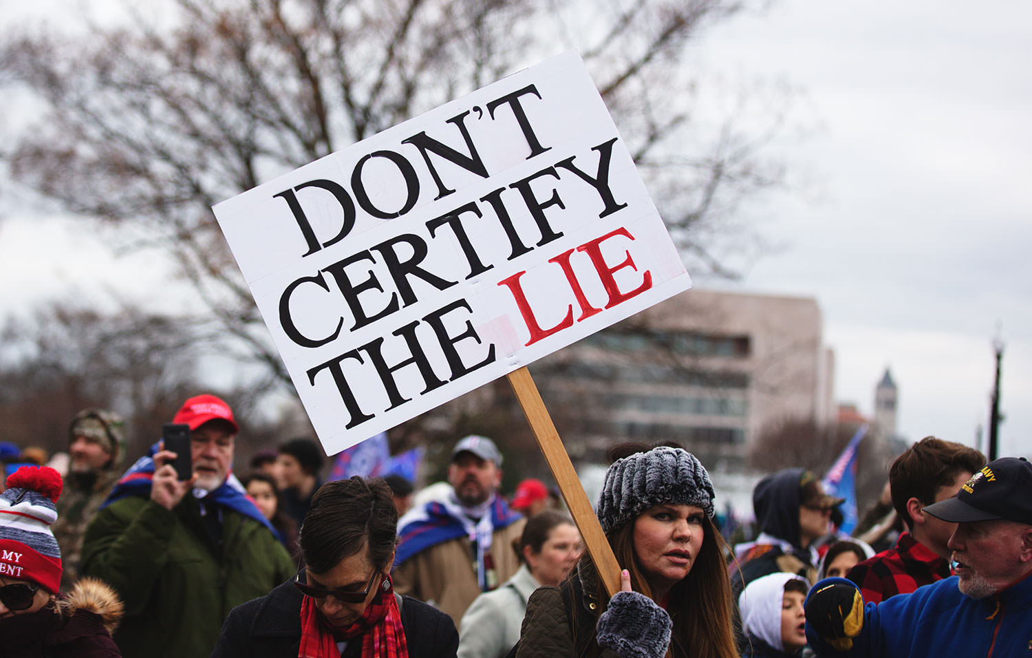 Woman holding a sign that reads "Don't certfiy the Lie"