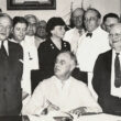 President Roosevelt signing the Social Security Act. Among those with the President are Senator Alben Barkley, Senator Robert Wagner, Senator Robert LaFollette, Secretary of Labor Frances Perkins, Representative Pat Harrison, and Representative David J. Lewis. August 14, 1935.