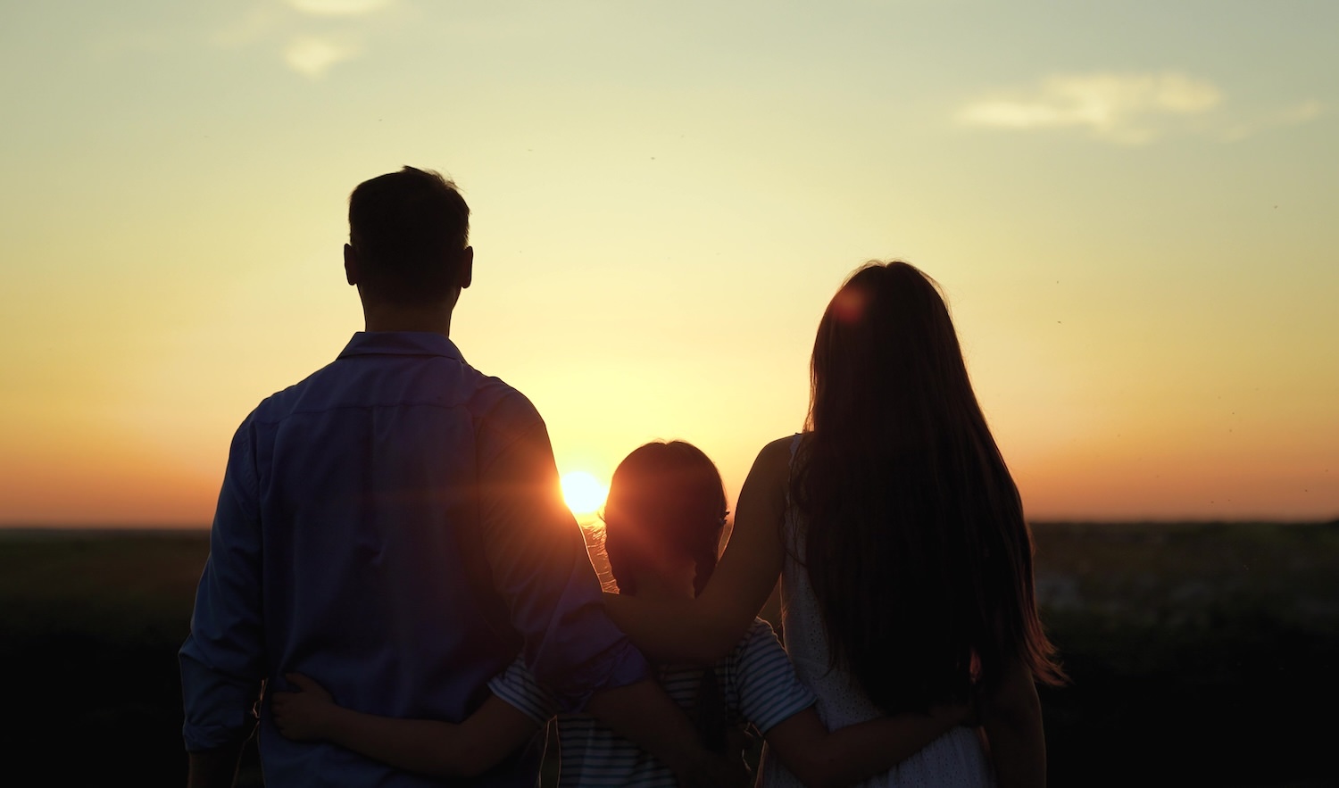 parents-child-Zoteva Mother and father with a child in silhouette with their backs to the viewer are looking at a sunset.