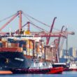 Port of Seattle, WA. Container ship Singapore Express with shipping containers under tow by two Crowley tug boats in harbor.